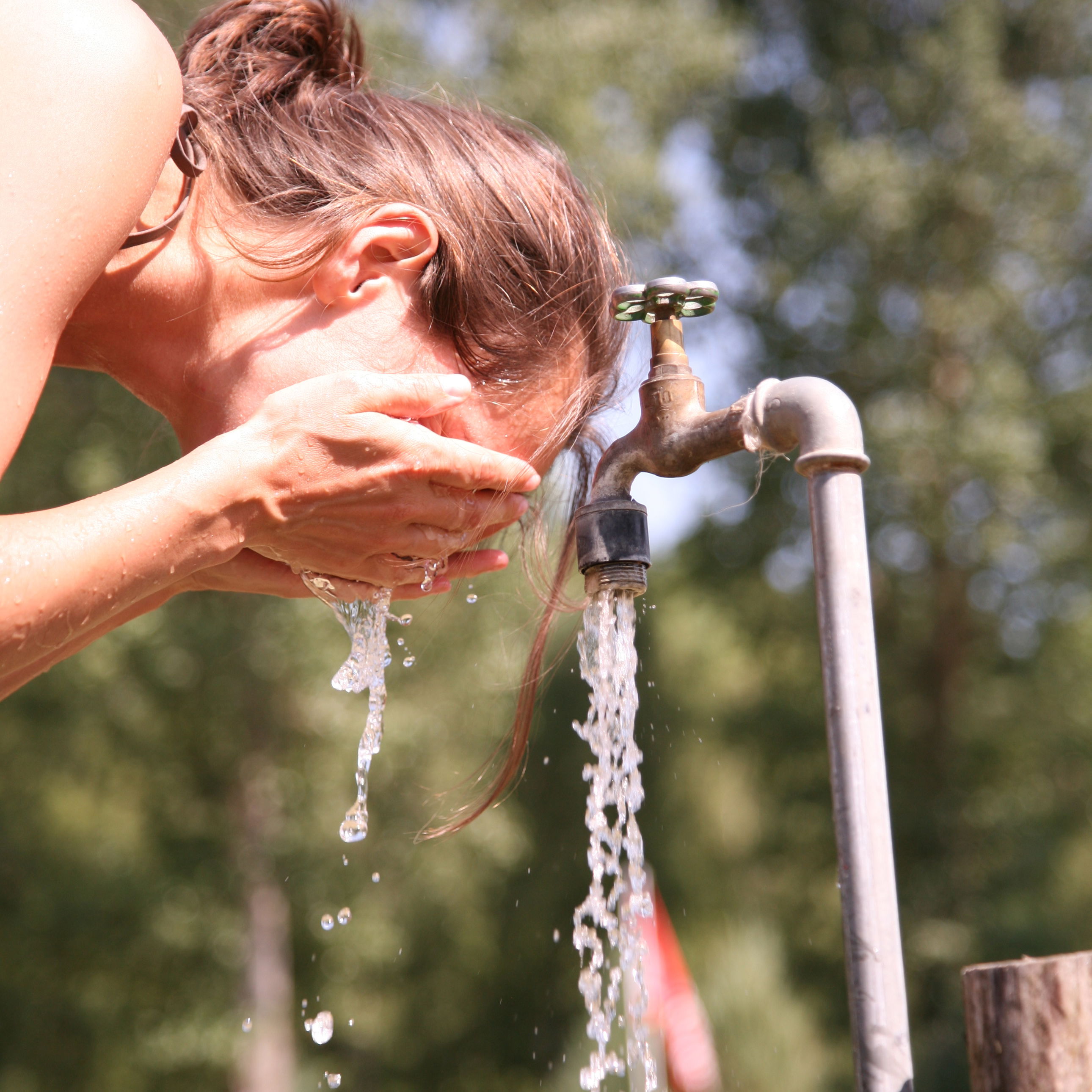 Kvinde vasker sig ansigt ved en udendørs vandhane