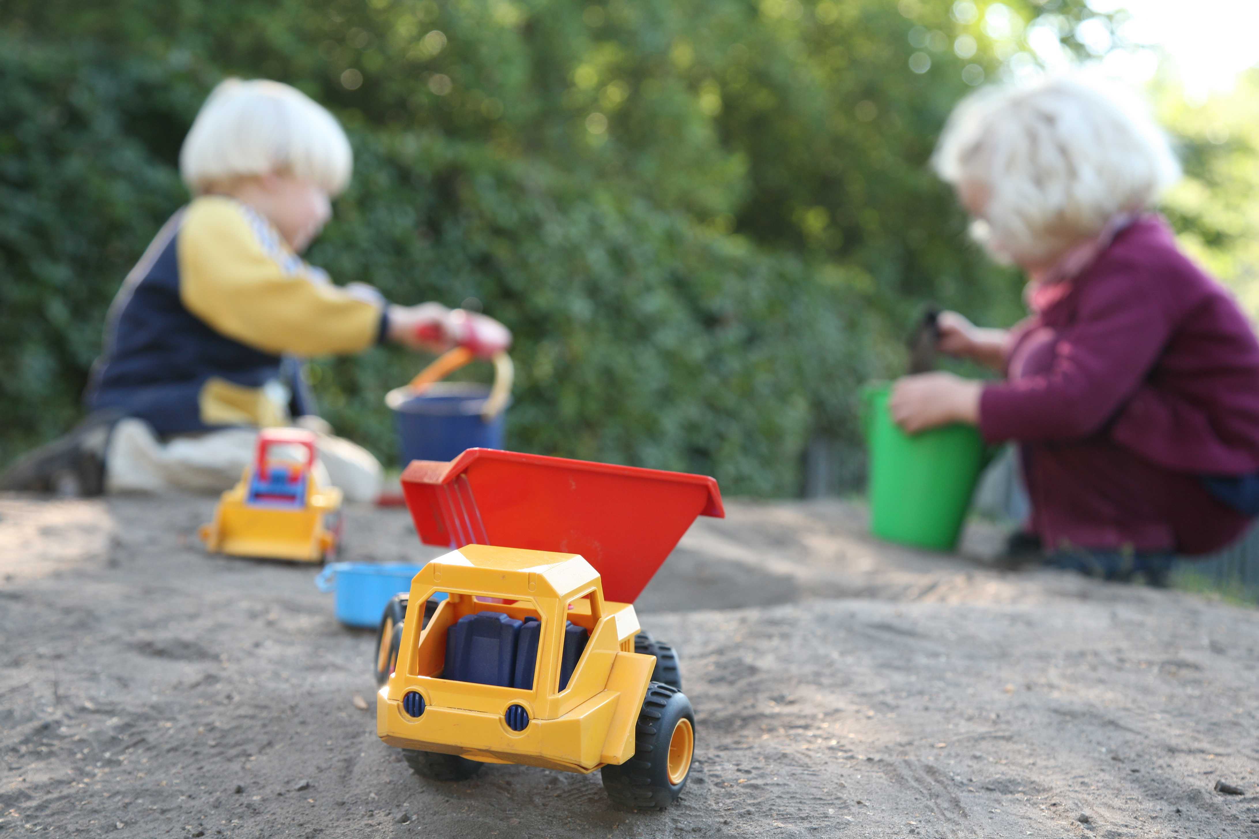Børn, der leger i en sandkasse. Der er spande og skovle, og der er også små legetøjsbiler.