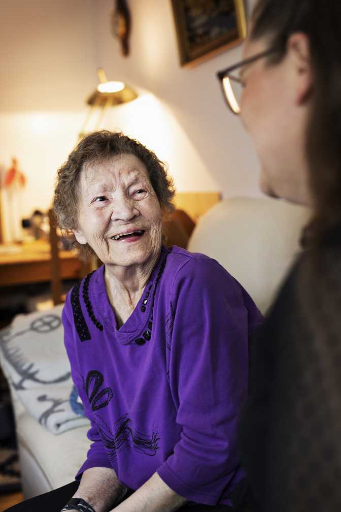 Ældre dame griner. Hun snakker med en SOSU-hjælper.