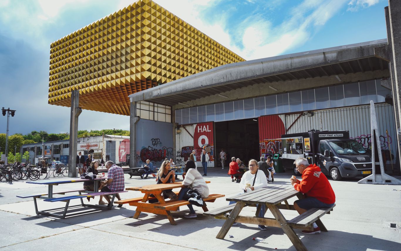 Folk sidder ved bænke på Søjlepladsen foran Hal 9